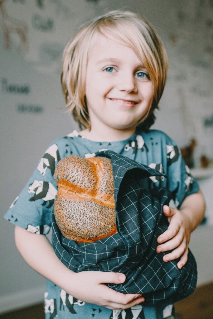pexels-photo-3730960-3730960 Happy young child holding a loaf of traditional bread indoors. Warm and inviting atmosphere.