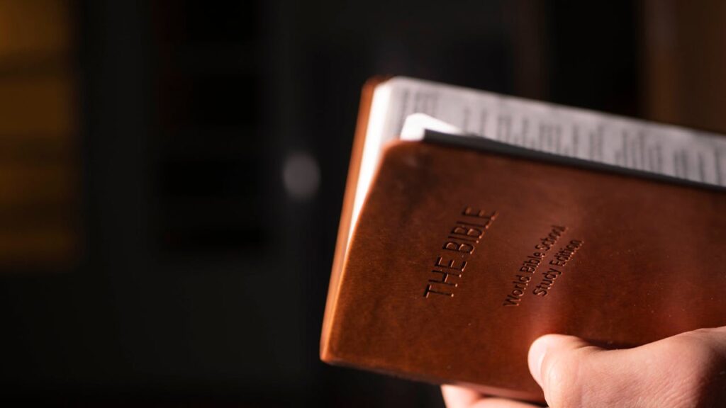 Close-up view of a hand holding a leather-bound Bible, featuring selective focus.
