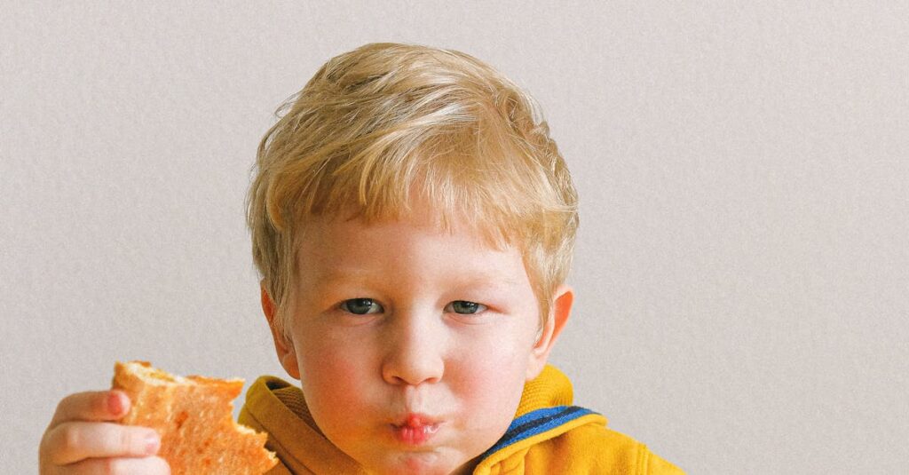 Young blond child in a yellow hoodie enjoying pizza and a drink at a table indoors. Cute and joyful moment.