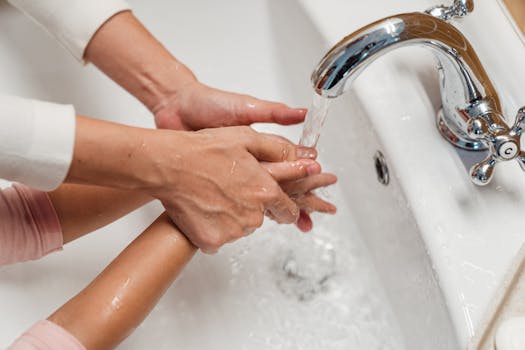 Focus on hygiene as a parent helps their child wash hands under a tap.