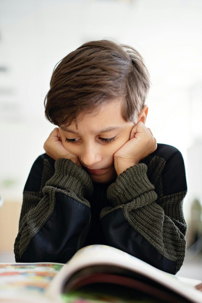 A young child in deep thought while reading a book in a classroom environment.